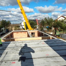 Usługi ogólnobudowlane Adaś - Budowa domu: widok z góry na wznoszone ściany z czerwonej cegły Porotherm, z dźwigiem w tle i pracownikiem w odblaskowej kamizelce, palety z cegłami na pierwszym planie.