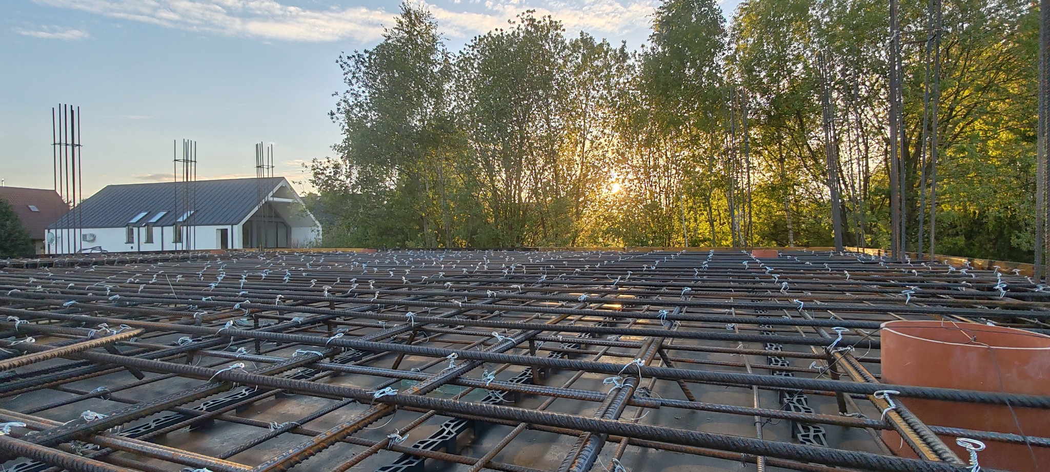Zbrojenie płyty fundamentowej domu jednorodzinnego w promieniach zachodzącego słońca, widok z bliska na siatkę stalową z elementami dystansowymi.
