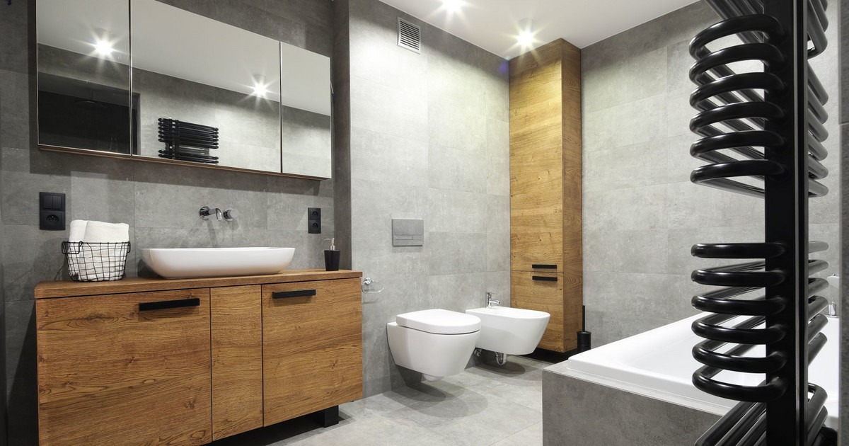 Nowoczesna łazienka z szarymi płytkami, drewnianą szafką pod umywalką, wiszącą toaletą i bidetem oraz spiralnym grzejnikiem w kolorze czarnym