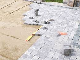 Fragment układanej powierzchni z szarej kostki brukowej, widoczny poziomica, przygotowane podłoże z piasku i geowłókniny, częściowo ułożona kostka w regularny wzór.