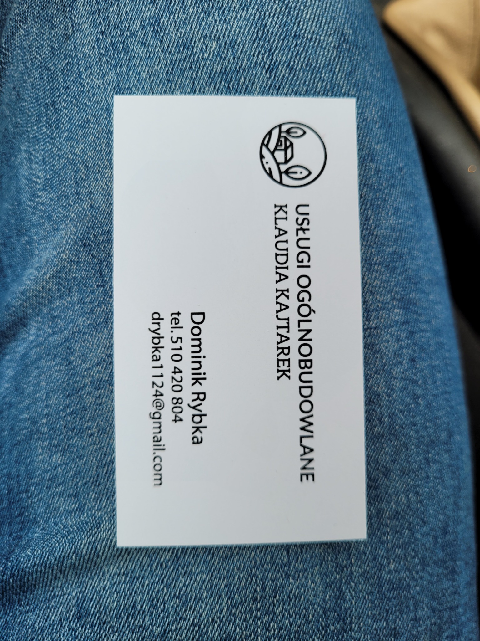 Wizytówka firmy z Wrocławia oferującej usługi ogólnobudowlane, leżąca na tle dżinsu. Na wizytówce widnieje logo oraz dane kontaktowe: imię, nazwisko, numer telefonu i adres e-mail.