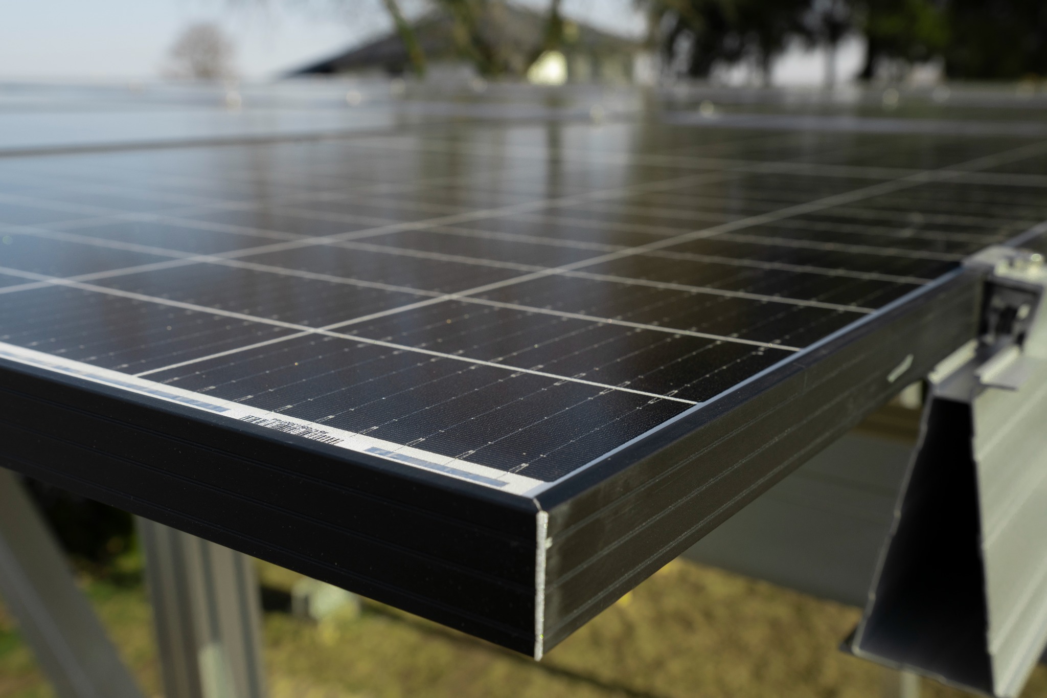 Szczegółowe ujęcie krawędzi panelu fotowoltaicznego na metalowej konstrukcji, widoczne złączenia i elementy mocujące, tło rozmyte.