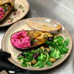 Elegancko podane danie: grillowany bakłażan z r&oacute;żowym musem buraczanym, granatem, oliwkami i sałatką z roszponki, serwowane z grzanką na talerzu w restauracji.