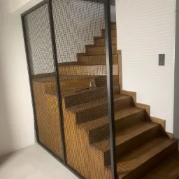 Drewniane schody z metalową siatką ochronną, widok z dołu, nowoczesny design, białe ściany i płytki podłogowe.