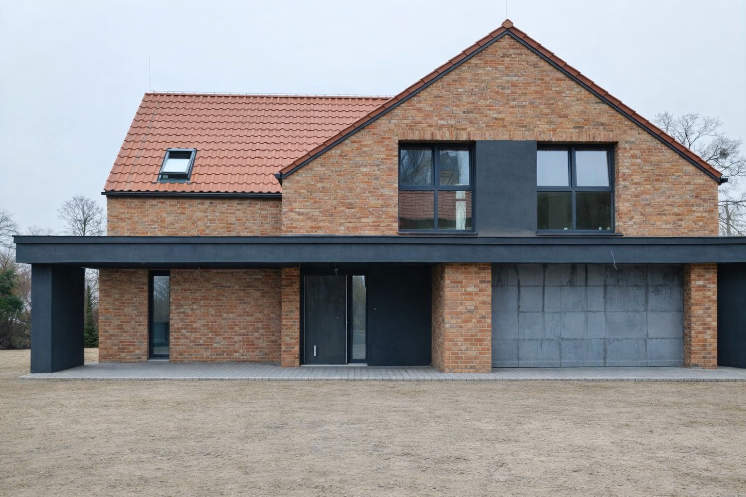Dwukondygnacyjny dom z cegły klinkierowej z garażem i płaskim dachem nad parterem. Czerwona dachówka, okna w ciemnych ramach. Surowy stan otoczenia.