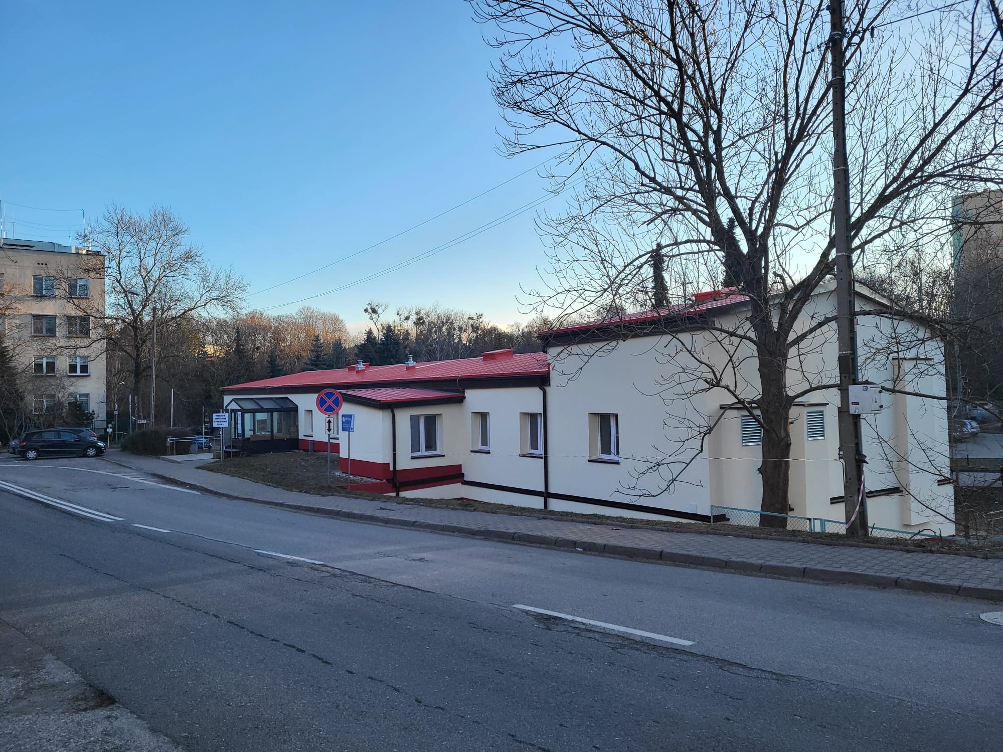 Budynek po remoncie z czerwoną dachówką i elementami wykończeniowymi, widoczny z ulicy w pochmurny dzień. Na pierwszym planie asfaltowa droga.