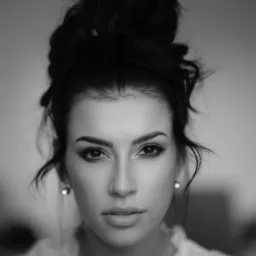 Portret kobiety z upiętymi włosami i delikatnym makijażem, czarno-białe zdjęcie z wyraźnym skupieniem na oczach i subtelnym oświetleniu.