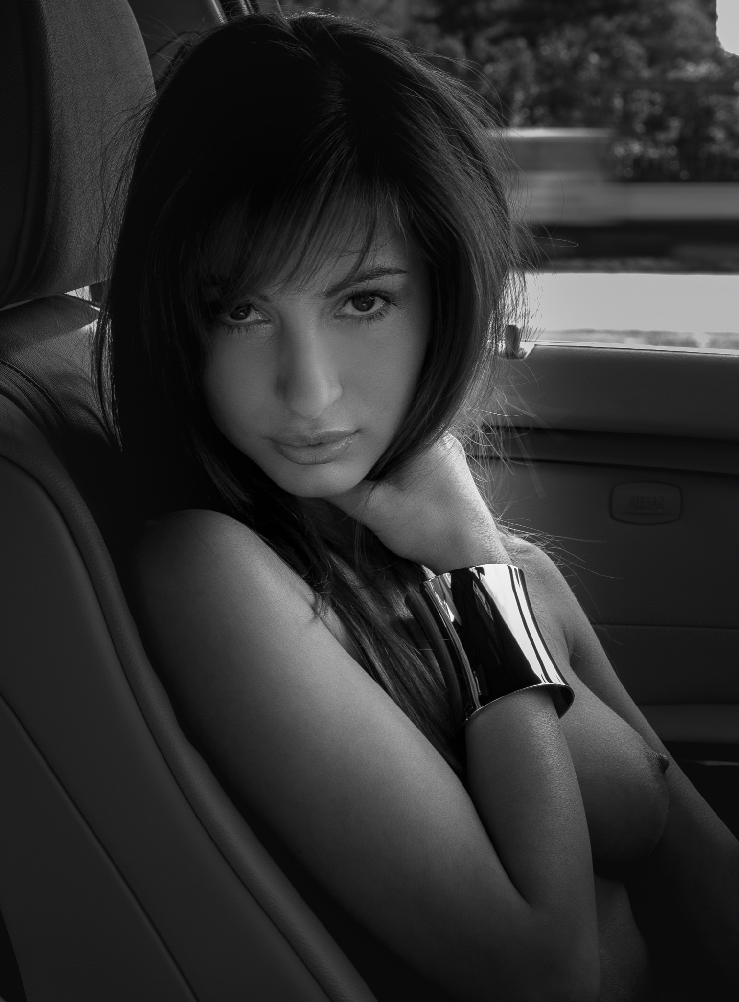 Portret kobiety w samochodzie, czarno-białe zdjęcie z mocnym oświetleniem, na ramieniu metalowa bransoleta.