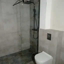 Nowoczesna łazienka z kabiną prysznicową typu walk-in z czarną armaturą i podwieszaną toaletą w kolorze białym, wykończona płytkami w odcieniach szarości.