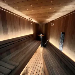 Wnętrze sauny wykończonej drewnem z podświetlanym sufitem imitującym gwiazdy, widoczne ławy, piec i akcesoria do sauny.