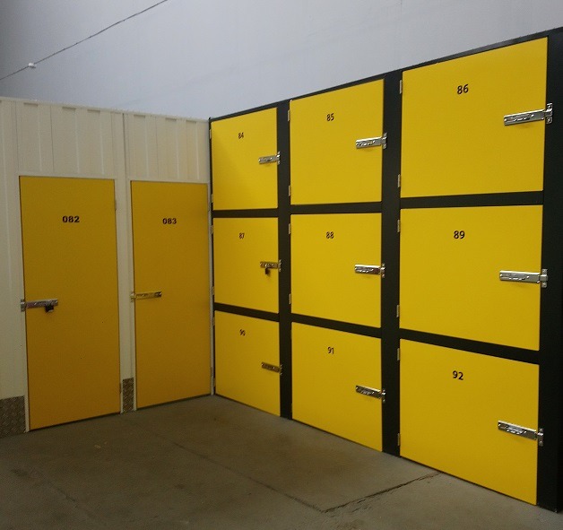Żółte, numerowane skrytki magazynowe z metalowymi zamkami, ustawione w rzędach w pomieszczeniu o jasnych ścianach.