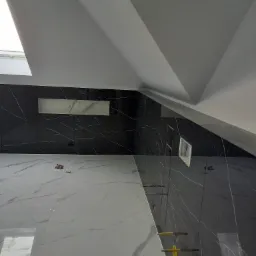 Ściana i podłoga w łazience wyłożone płytkami imitującymi marmur, widoczne elementy montażowe, wnęka w ścianie pod skosem dachu.