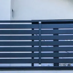 Szare, poziome panele balkonowe zamontowane na budynku z białymi ścianami i ciemnymi oknami oraz dachem.