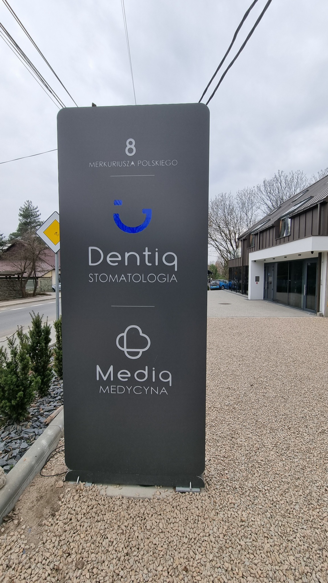Szyld reklamowy przed budynkiem: Dentiq Stomatologia i Media Medycyna, adres 8 Merkuriusza Polskiego.
