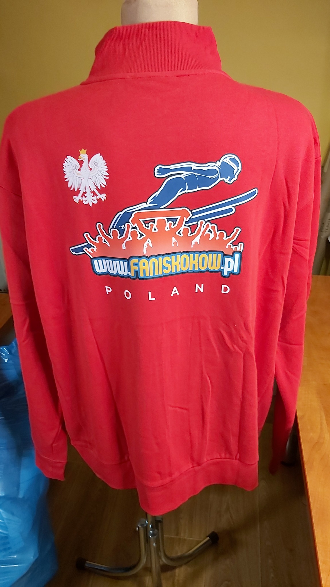 Czerwona bluza z nadrukiem skoczka narciarskiego, orła i napisu www.faniskokow.pl POLAND, prezentowana na manekinie.