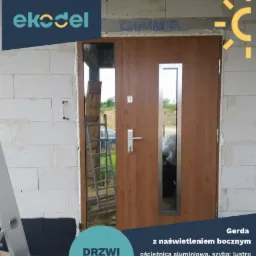 Brązowe drzwi zewnętrzne z bocznym naświetleniem i lustrem weneckim, zamontowane w surowym murze z betonu komórkowego, widoczna drabina i logo firmy Eko-del.