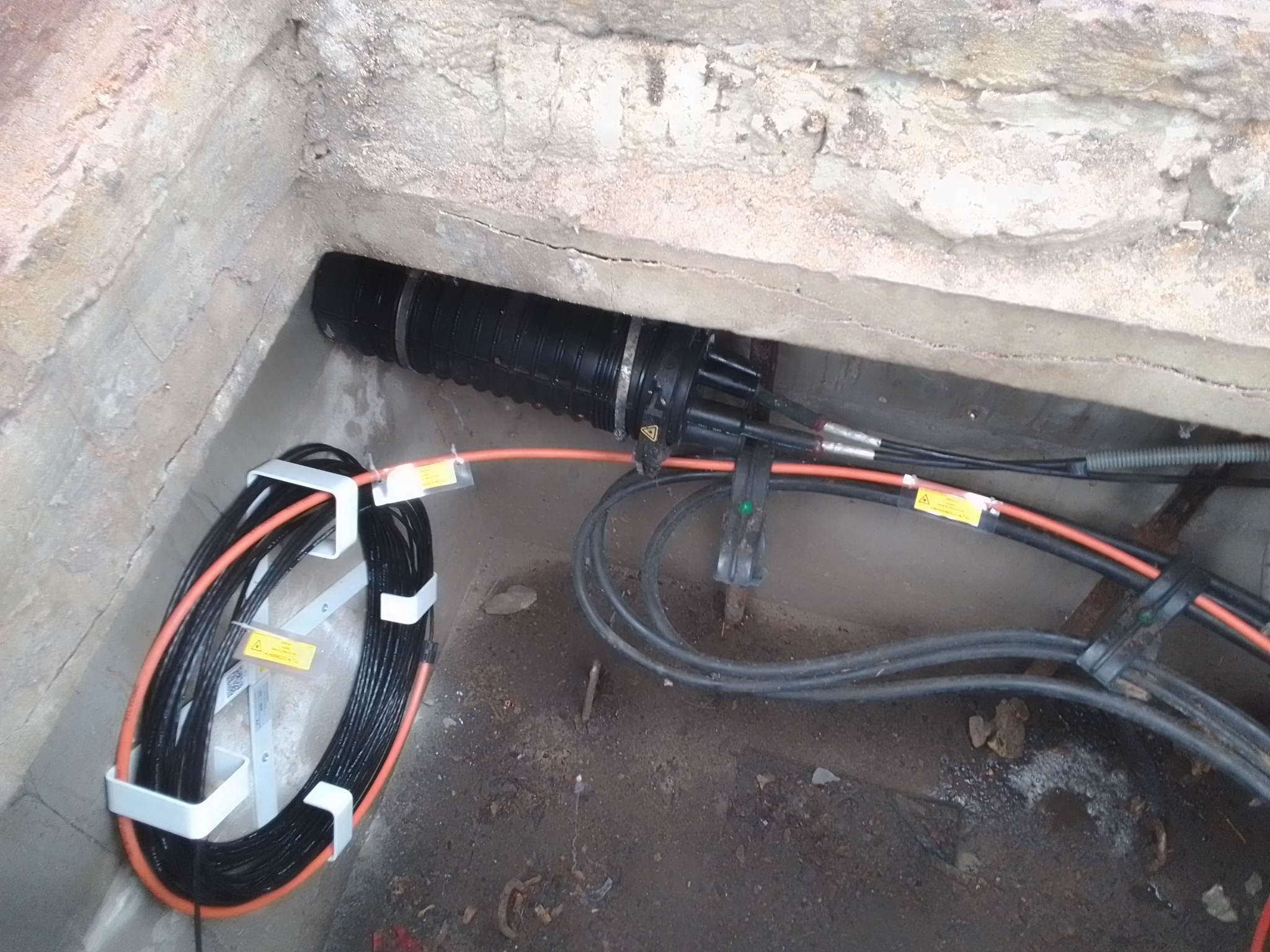 Studzienka telekomunikacyjna z kablem światłowodowym na uchwycie, widoczne złącze kablowe. Prace instalacyjne w Warszawie.