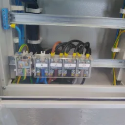 Wnętrze skrzynki elektrycznej z widocznymi przewodami, listwami zaciskowymi oznaczonymi N, L1, L2, L3, oraz elementami montażowymi na szynach DIN.