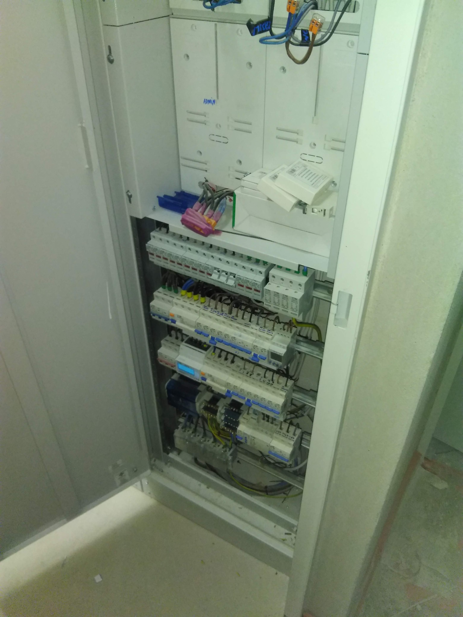 Otwarta szafa elektryczna z widocznymi bezpiecznikami, wyłącznikami różnicowoprądowymi, przewodami i złączkami WAGO, częściowo zamontowana, z napisem 'ADMIN' na obudowie.