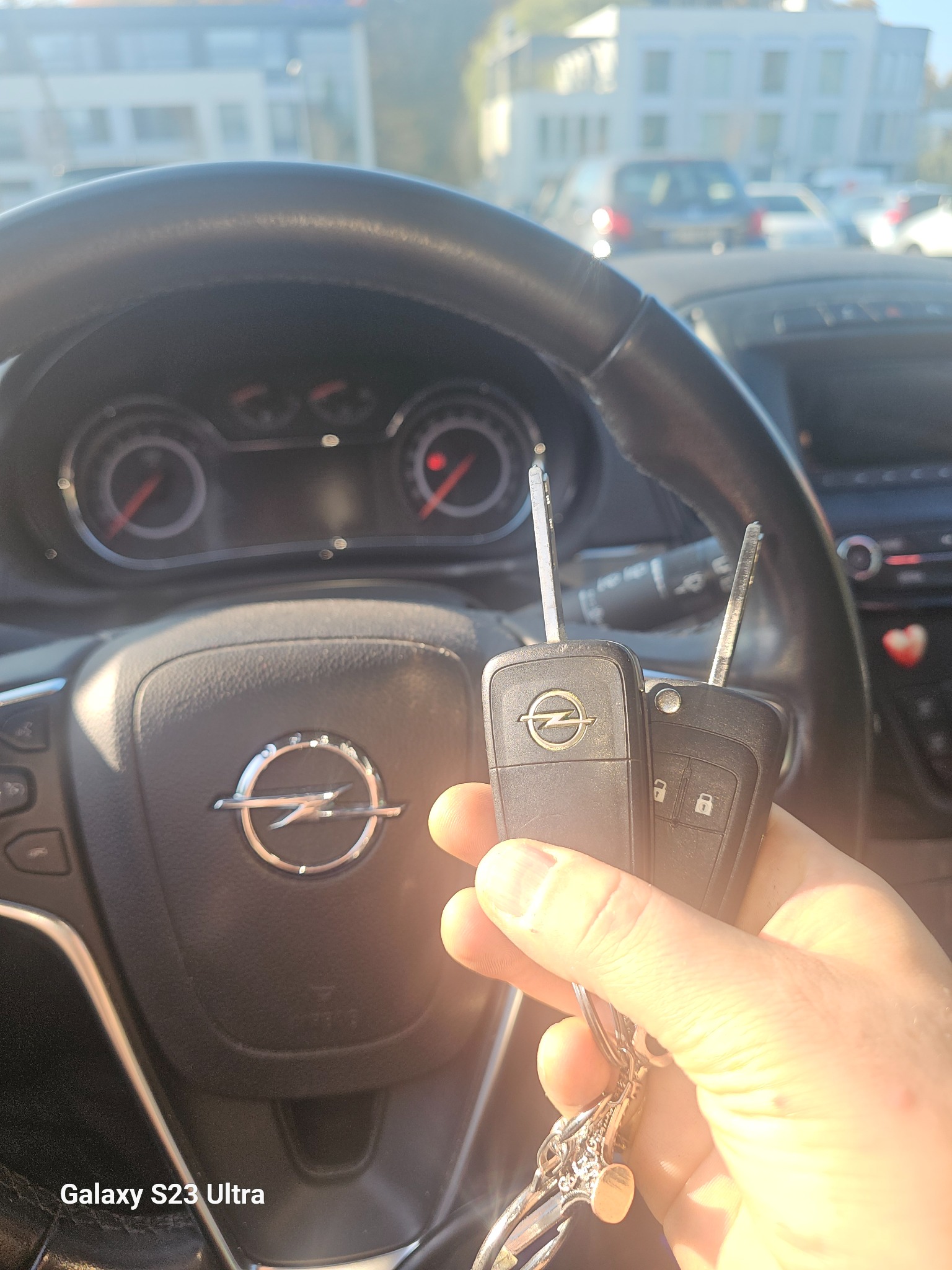 Dwa kluczyki samochodowe z logo Opla w dłoni na tle kierownicy i deski rozdzielczej Opla, widok z perspektywy kierowcy.