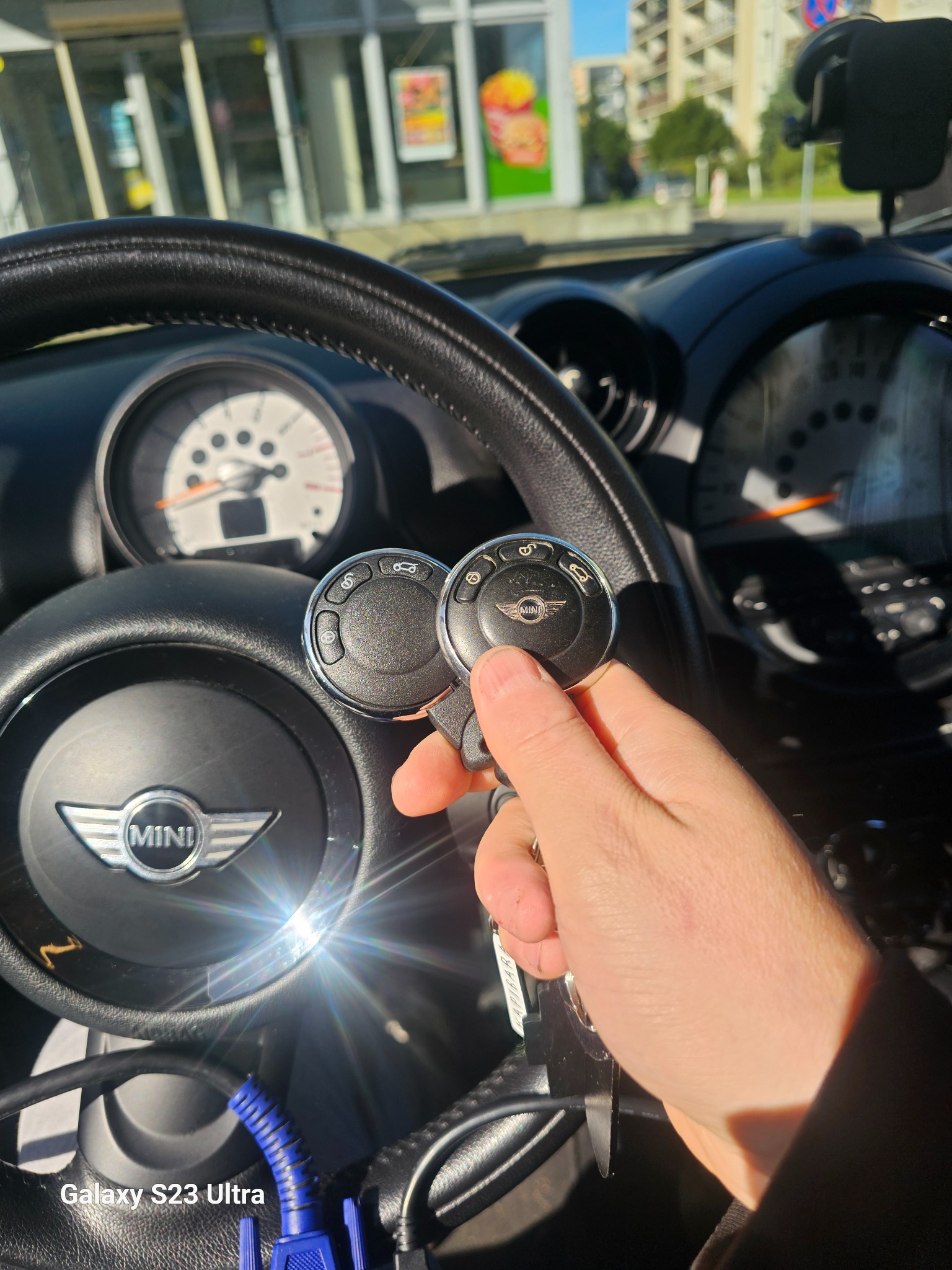 Wnętrze Mini Cooper z kluczykami w dłoni, deska rozdzielcza i kierownica widoczne. Kluczyki z logo Mini, diagnostyka samochodowa w tle.