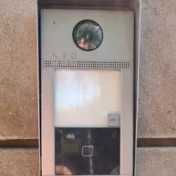 Zamontowany na szarej ścianie wideodomofon Hikvision z widoczną kamerą, mikrofonem i czytnikiem kart zbliżeniowych.