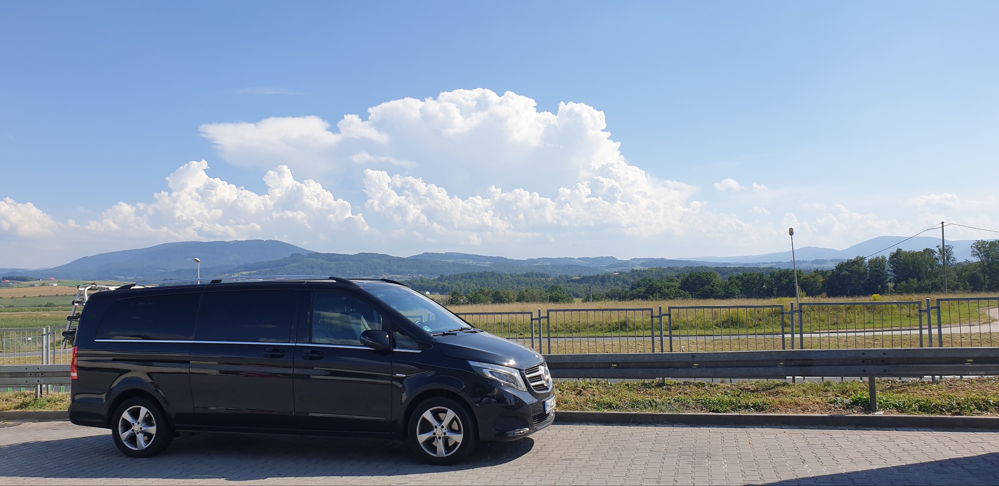 Czarny van Mercedes z bagażnikiem rowerowym na dachu, zaparkowany w Złotoryi z widokiem na góry i błękitne niebo z obłokami.