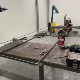 Stół spawalniczy z ramą z profili stalowych w trakcie spawania. Widoczne narzędzia, spawarka, pochłaniacz pyłów spawalniczych oraz skrzynka narzędziowa.