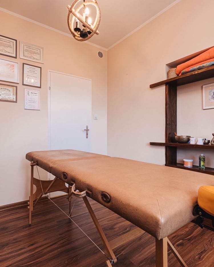 Brązowy stół do zabiegów w gabinecie z certyfikatami na ścianie i lampą w stylu marynistycznym.