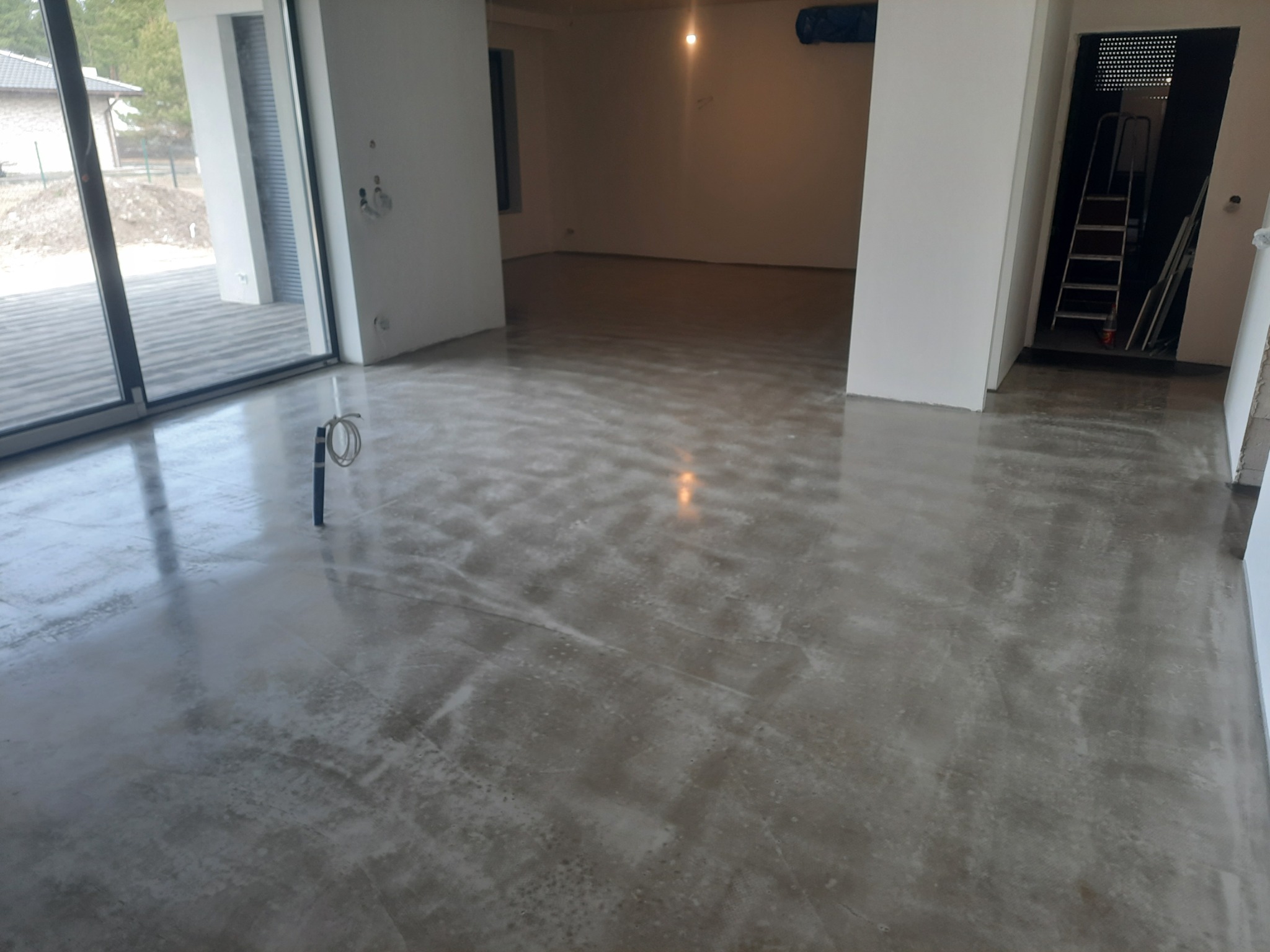 Wnętrze w stanie deweloperskim, widoczna wylewka anhydrytowa na podłodze, przygotowana do dalszych prac wykończeniowych, widoczne ślady po szlifowaniu, w tle drabina i otwarte przestrzenie