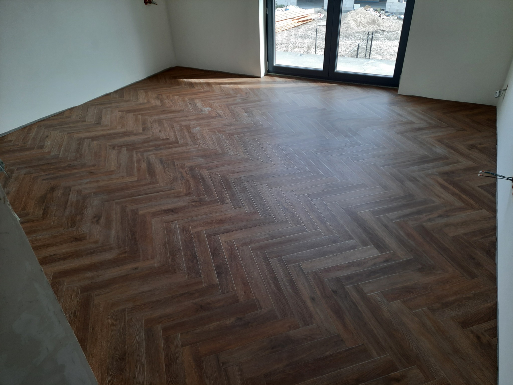 Ułożony parkiet w jodełkę francuską w nowym pomieszczeniu, widok na okno balkonowe i świeżo pomalowane ściany.