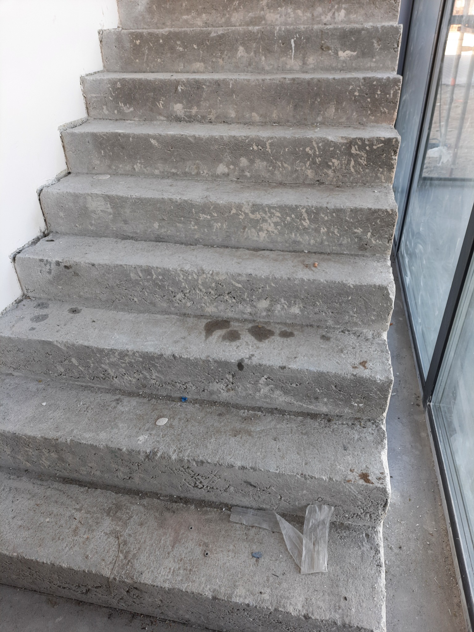 Surowe, betonowe schody wewnętrzne w trakcie budowy, widoczne niedoskonałości powierzchni i resztki budowlane.