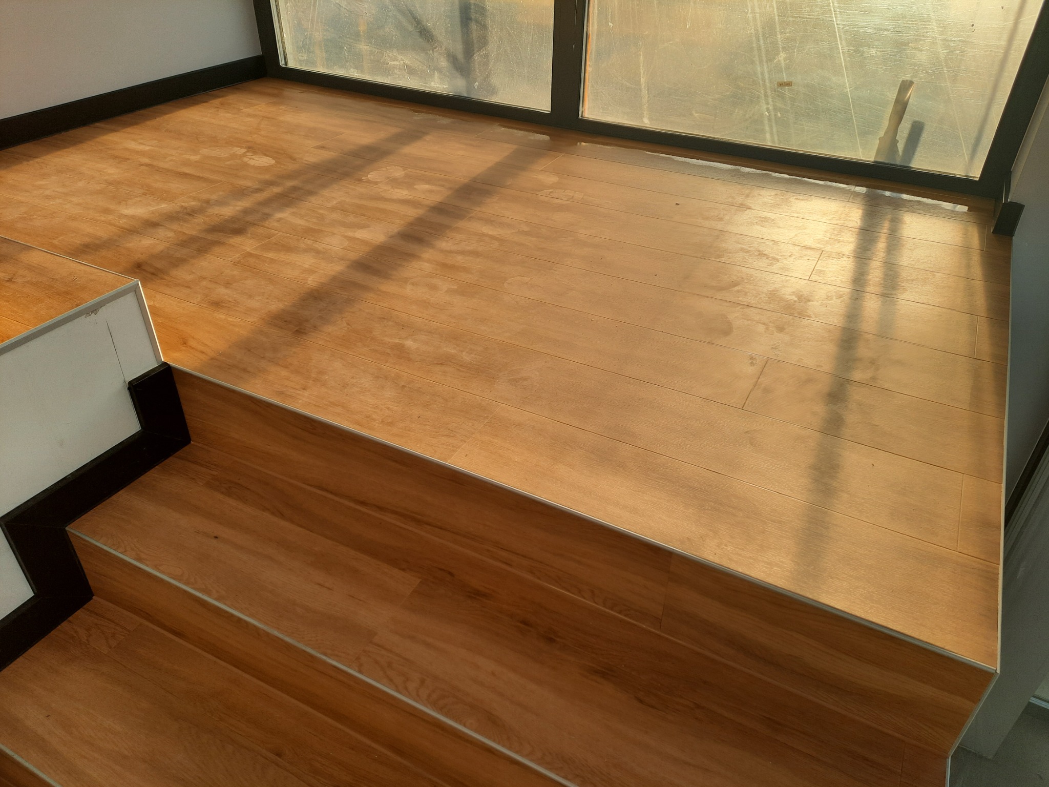 Jasne panele podłogowe, ułożone na podłodze i schodach w pobliżu okna, widoczne ślady użytkowania.