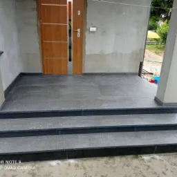 Wykończone schody wejściowe i taras przed domem, z szarych płyt kamiennych, widoczne niedokończone elementy elewacji.