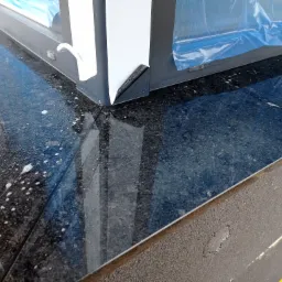 Czarny, błyszczący parapet kamienny z resztkami folii ochronnej i śladami czyszczenia po montażu.