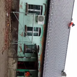 Pracownik w pomarańczowej kamizelce na dachu dwupiętrowego domu z blachodachówką, widoczne rusztowanie i odpadający tynk na elewacji budynku.