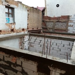 Magda Rzeszutek - Budowa domu: widok na fundamenty i ściany w trakcie murowania z betonu komórkowego. Widoczne wystające pręty zbrojeniowe i fragmenty starej konstrukcji.