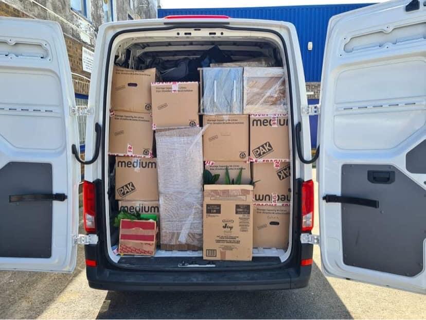 Wnętrze białego furgonetki załadowane kartonami z napisem 'medium' i 'PAK', zabezpieczonymi folią, widoczne otwarte tylne drzwi.