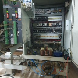 Intertech Krzysztof Łach - Otwarta szafa sterownicza maszyny przemysłowej z widocznymi elementami elektrycznymi, przewodami, transformatorami i multimetrem pomiarowym w prawym dolnym rogu.