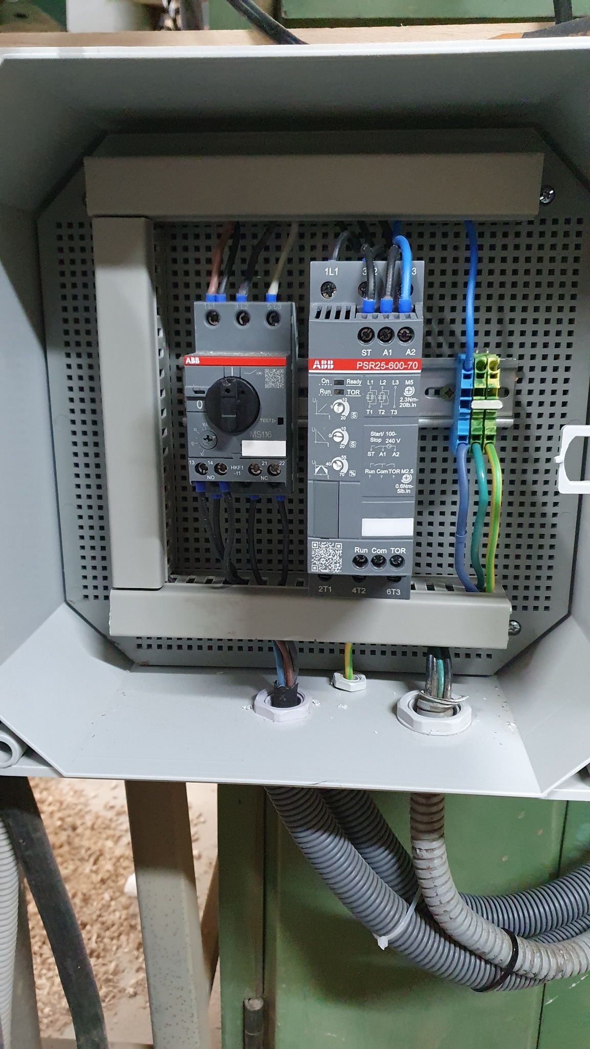 Wnętrze skrzynki elektrycznej z zamontowanymi stycznikami ABB MS116 i PSR25-600-70, widoczne przewody, listwa zaciskowa i peszle doprowadzające kable.