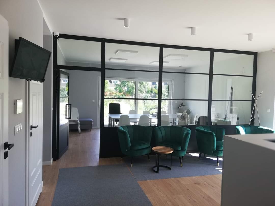 Jasne, nowocześnie urządzone wnętrze biura z zielonymi fotelami, szklaną ścianą oddzielającą przestrzeń konferencyjną i drewnianą podłogą.