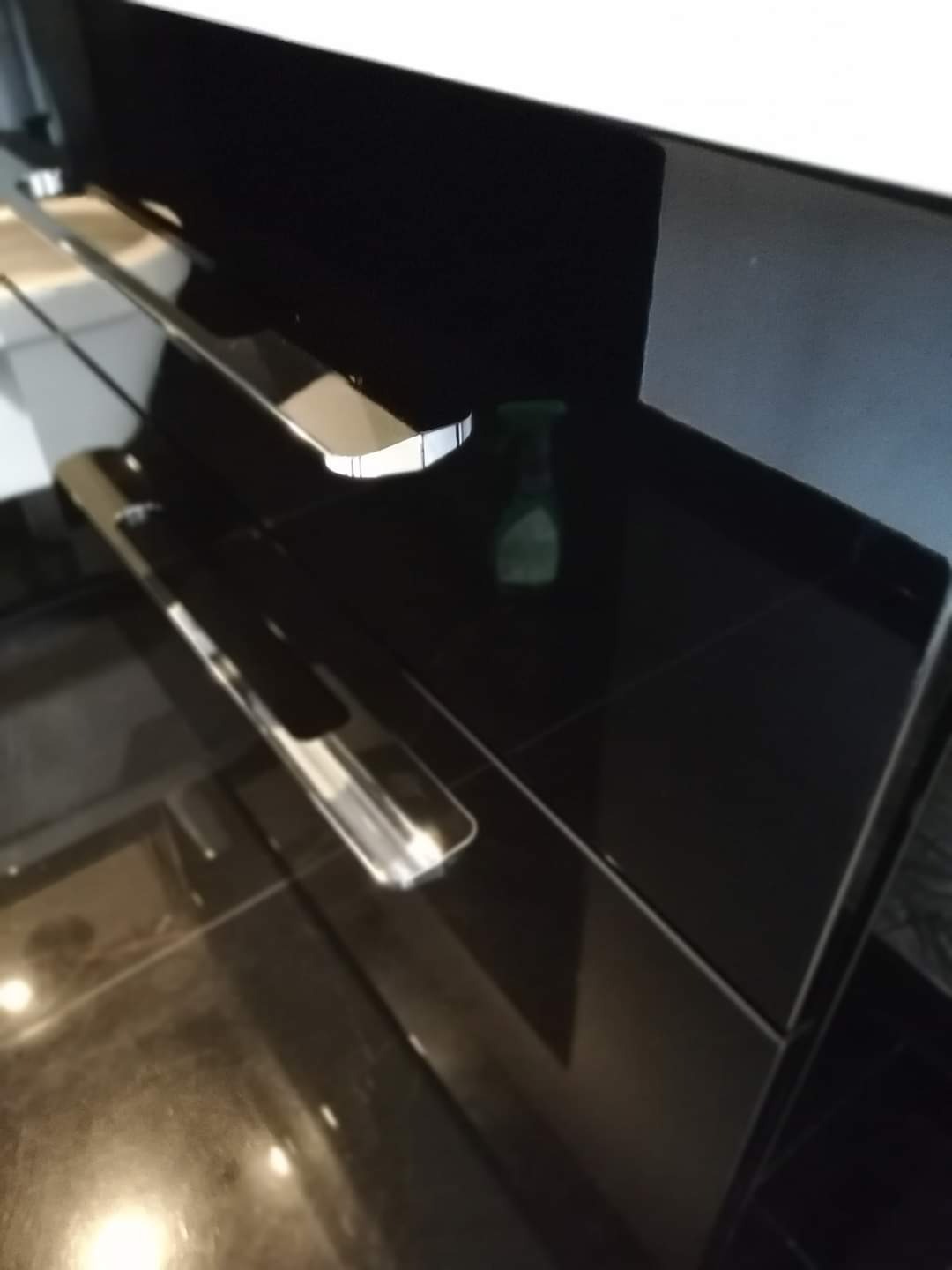 Błyszcząca, czarna powierzchnia blatu z widocznym odbiciem i butelką środka czyszczącego w tle, podkreślająca efekt po umyciu.