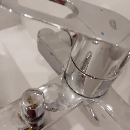 Chromowana bateria umywalkowa Grohe z widocznymi śladami kamienia i zaciekami, ustawiona na białej umywalce, sfotografowana z bliska pod kątem.