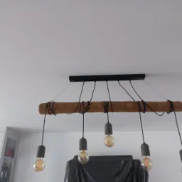 Drewniana lampa wisząca z sześcioma żarówkami Edison, zamontowana na czarnej listwie podsufitowej, widoczna na tle białego sufitu i fragmentu zabudowy kuchennej.