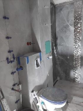 Szara łazienka w trakcie remontu w Warszawie. Widoczne płytki imitujące marmur, niebieskie krzyżyki glazurnicze i zabudowa stelaża WC przed montażem ceramiki.