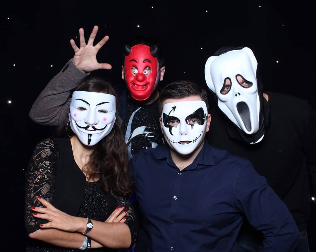Grupa czterech osób w maskach (Anonymous, diabeł, Scream, Joker) pozuje na tle ciemnego tła z gwiazdkami.