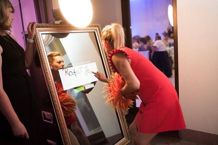 Kobieta w czerwonej sukience korzysta z interaktywnego lustra z ramą w stylu vintage, na ekranie widoczny napis 'Rafał Ja'.