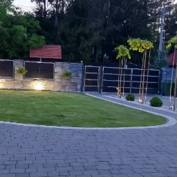 Nowoczesne ogrodzenie panelowe z podświetleniem LED, r&oacute;wno przystrzyżony trawnik i elegancka kostka brukowa tworzą zadbany krajobraz posesji.