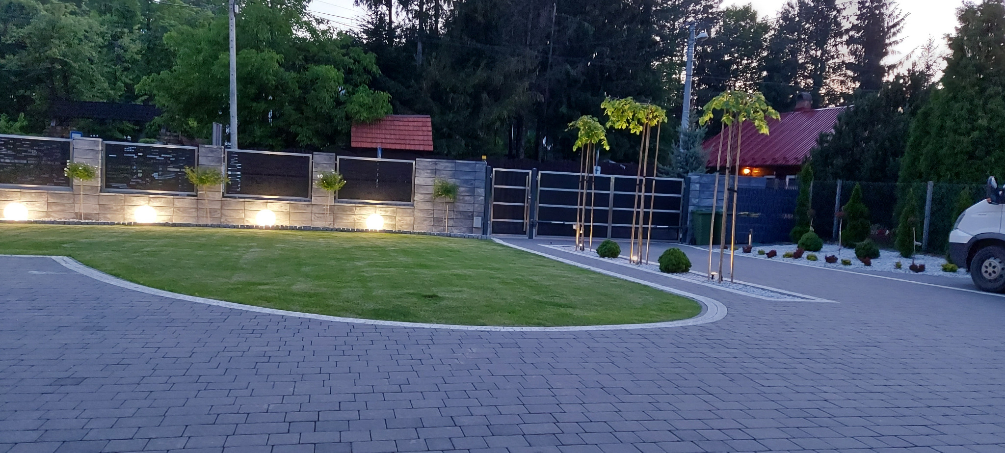 Nowoczesne ogrodzenie panelowe z podświetleniem LED, równo przystrzyżony trawnik i elegancka kostka brukowa tworzą zadbany krajobraz posesji.