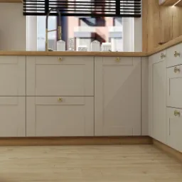 Jasna kuchnia z drewnianymi akcentami, złotymi gałkami i ceglaną ścianą w tle, widok na okno z małymi modelami budynków.